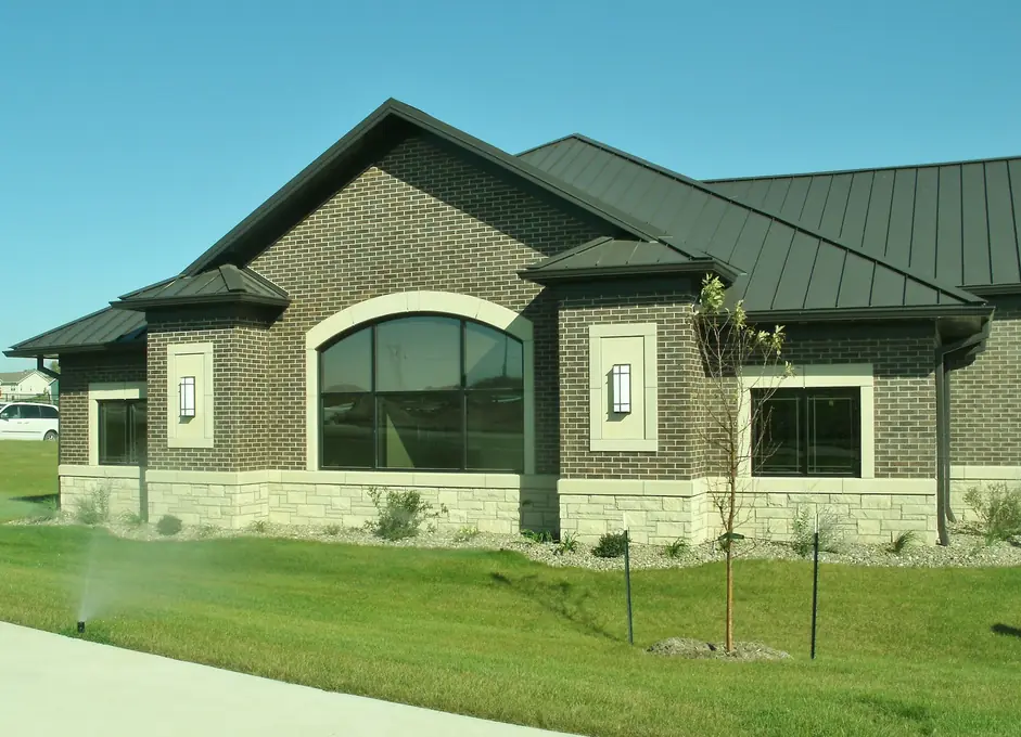 Sprinkler watering the lawn beside a brick commercial building with a green metal roof