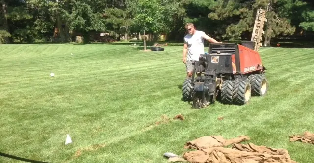 Fleming crew member running a pipe-pulling machine across a striped lawn
